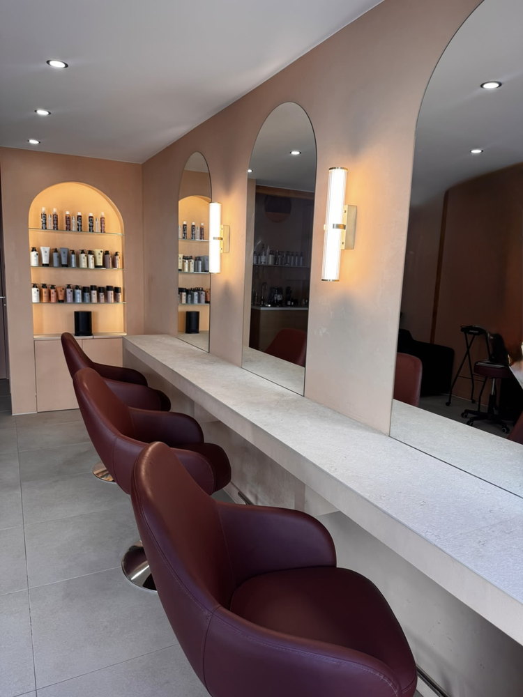 Le salon : fauteuils bordeaux alignés devant les miroirs en arche et la niche de soins rétroéclairée